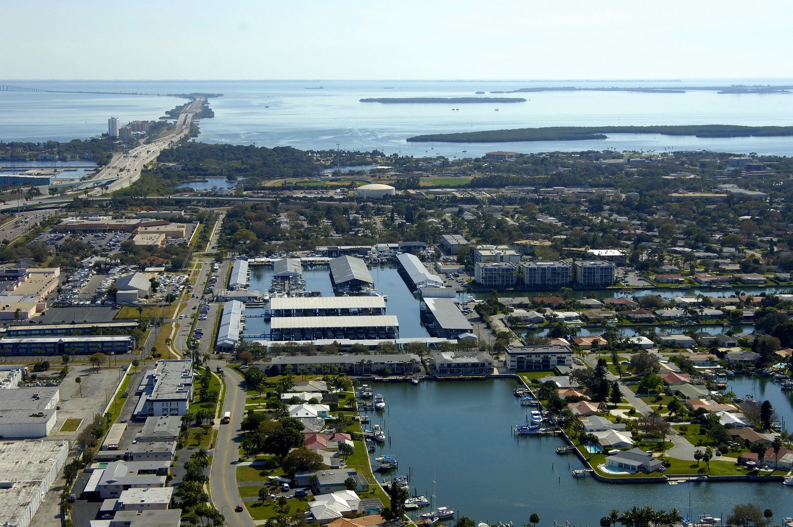 Aerial view over Maximo Marina and Boca Ciega Bay, St. Petersburg, with the covered slip rows in the foreground and the Sunshine Skyway in the distance.