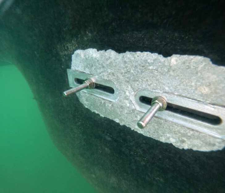 A heavily consumed sacrificial anode underwater, pitted and eroded down around its mounting studs