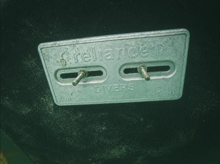 A fresh rectangular sacrificial anode bolted to a dark hull underwater, edges and lettering intact