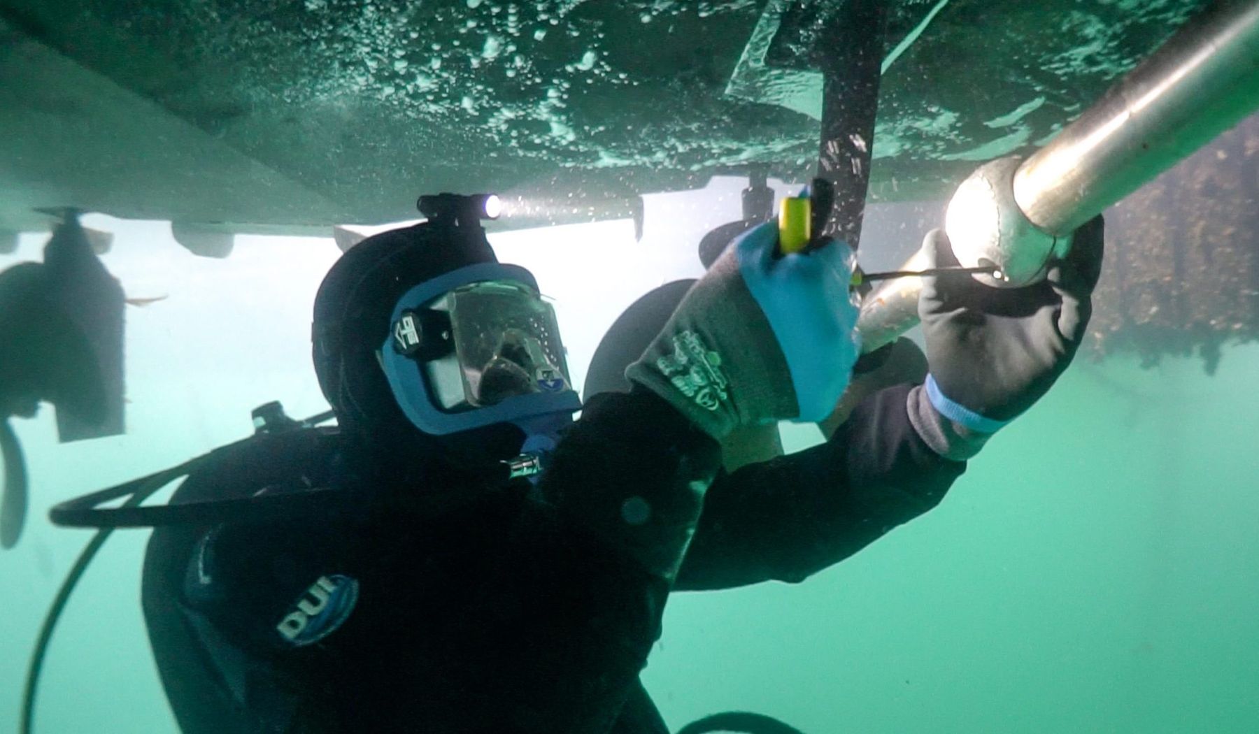 Diver working beneath a boat hull underwater